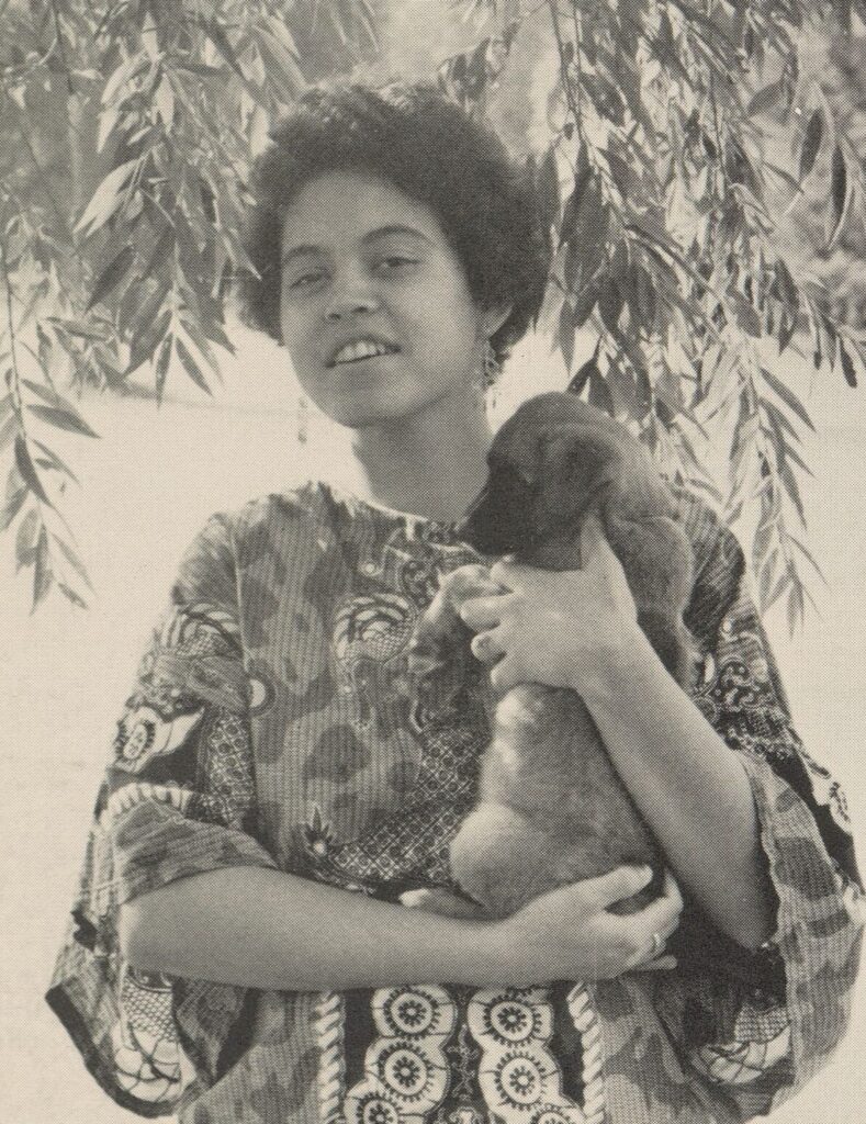 Yearbook photograph of Mindy Thompson. She wears a dashiki and Afro and is smiling and holding a small dog.